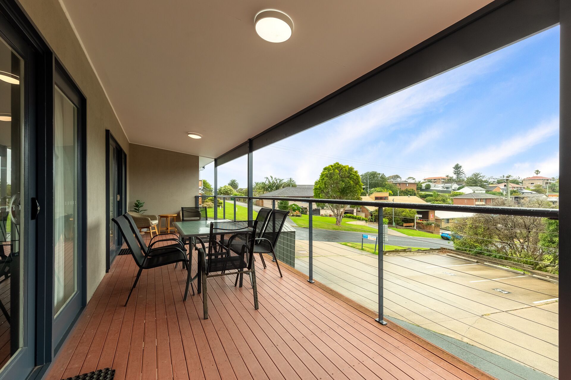 A balcony with a table and chairs, a view of a residential area, and a clear sky.