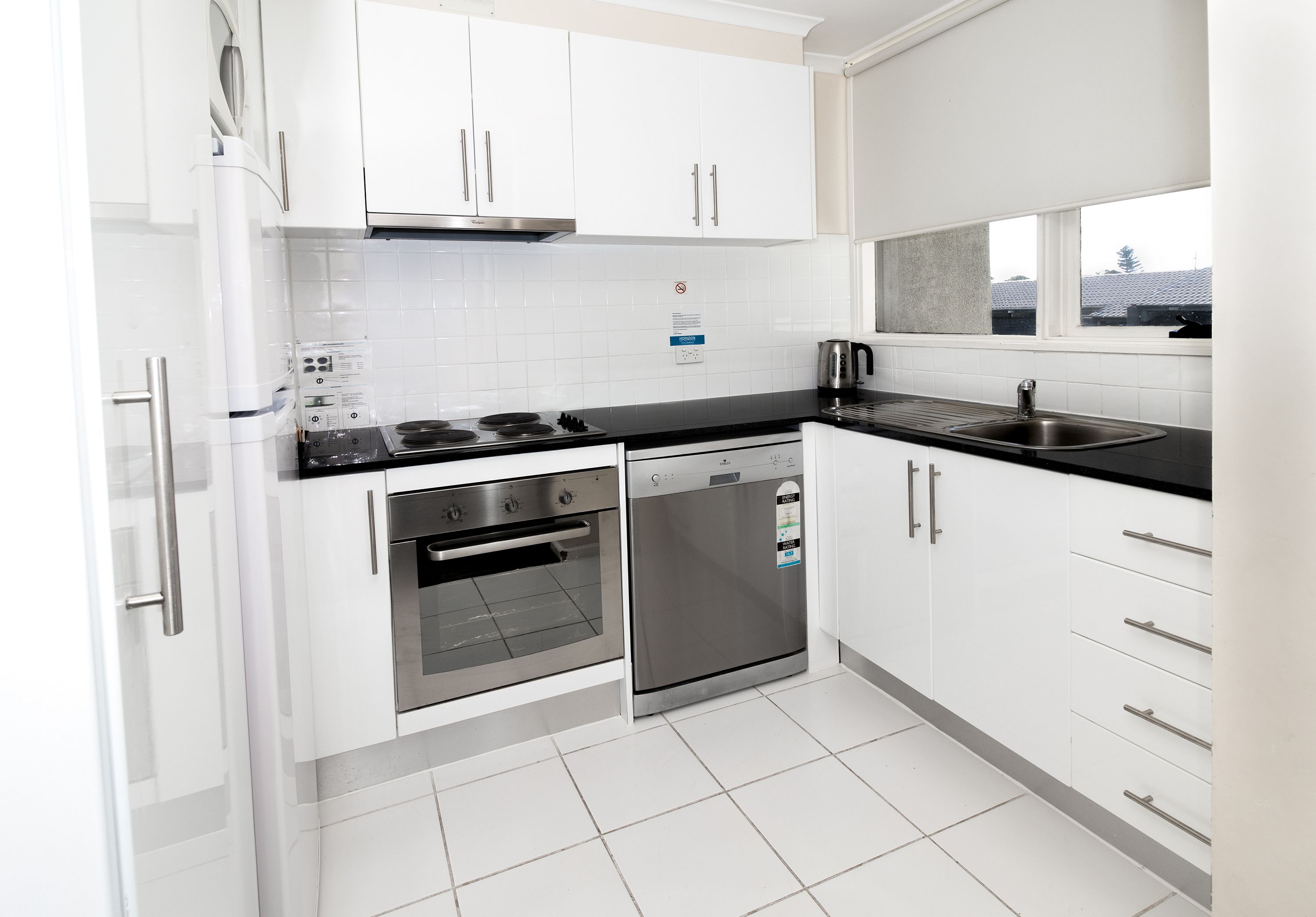 Una cocina moderna con armarios blancos, electrodomésticos de acero inoxidable y encimera negra.