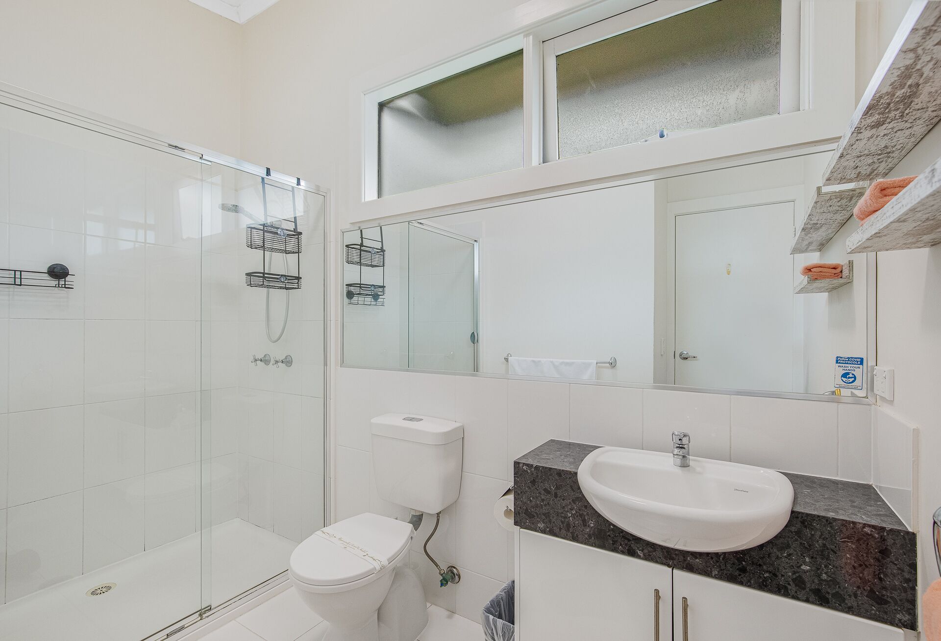 Un baño moderno con ducha de vidrio, inodoro, lavabo con encimera de granito y un espejo grande.