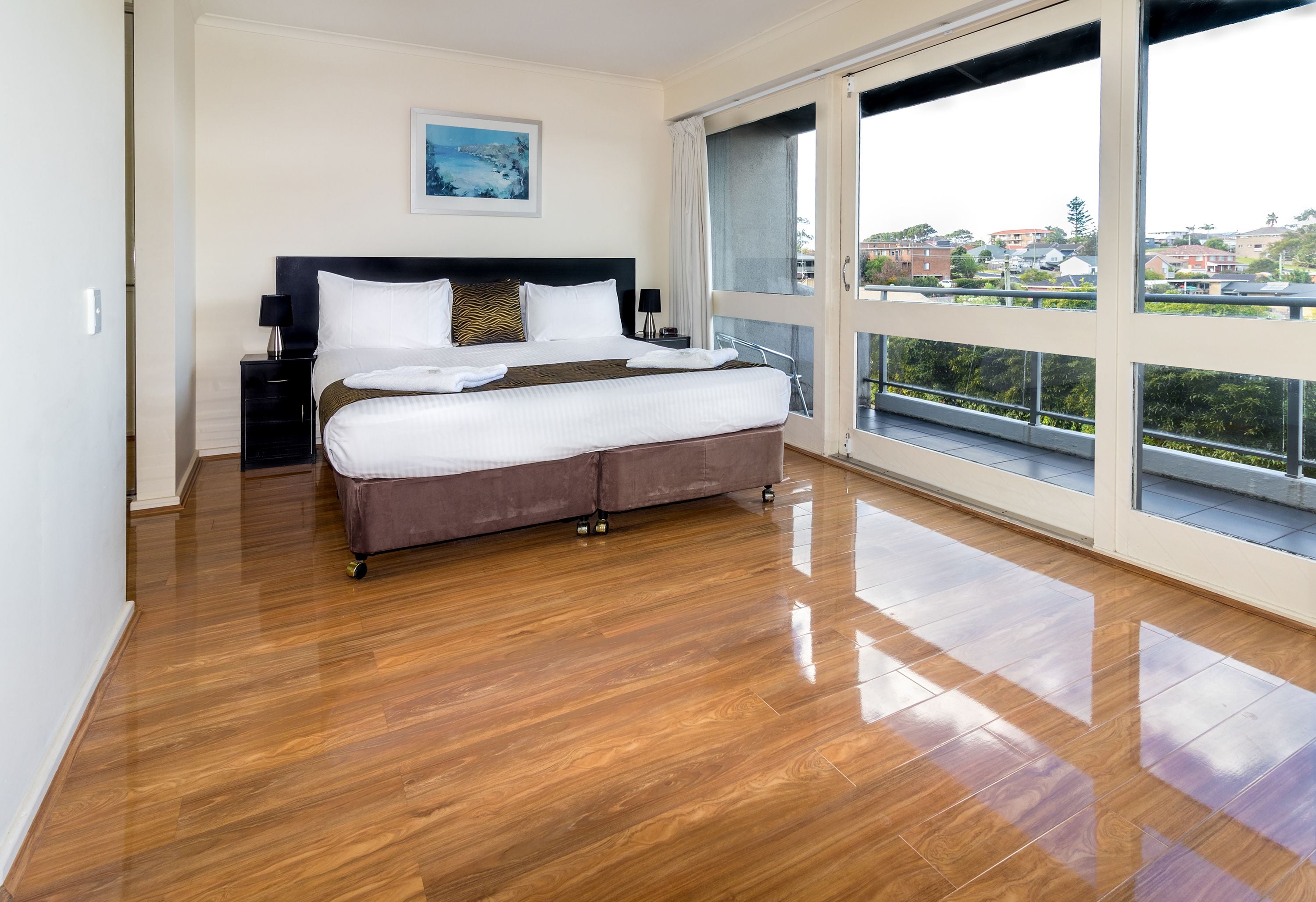 Une chambre à coucher avec un grand lit, une table de chevet, une fenêtre donnant sur des immeubles et un plancher en bois.
