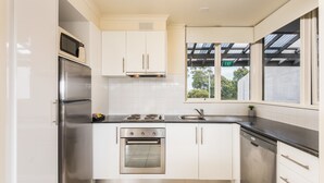 A modern kitchen with stainless steel appliances, white cabinets, and a window with an exit sign.