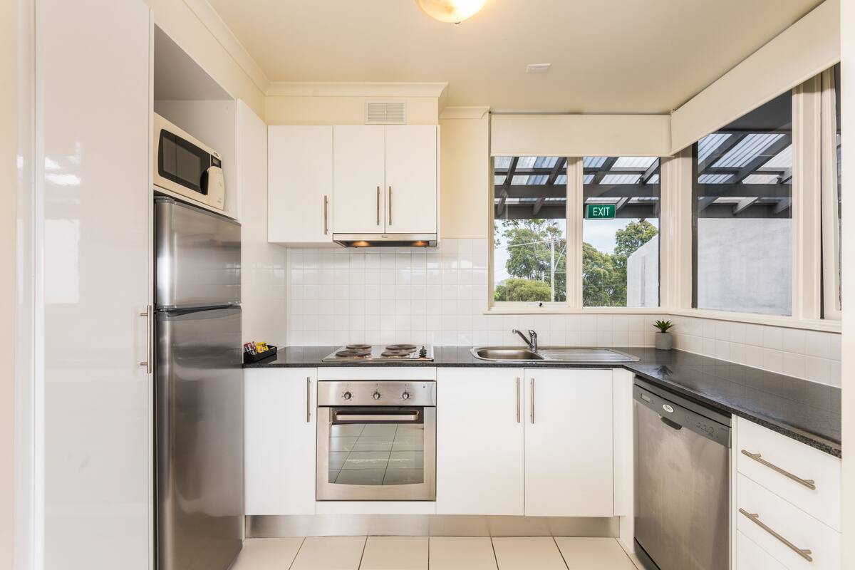 A modern kitchen with stainless steel appliances, white cabinets, and a window with an exit sign.