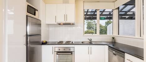 A modern kitchen with stainless steel appliances, white cabinets, and a window with an exit sign.