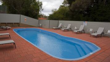 Une piscine rectangulaire aux parois bleues, entourée d’une terrasse en briques. On y trouve plusieurs chaises longues et une table de pique-nique.