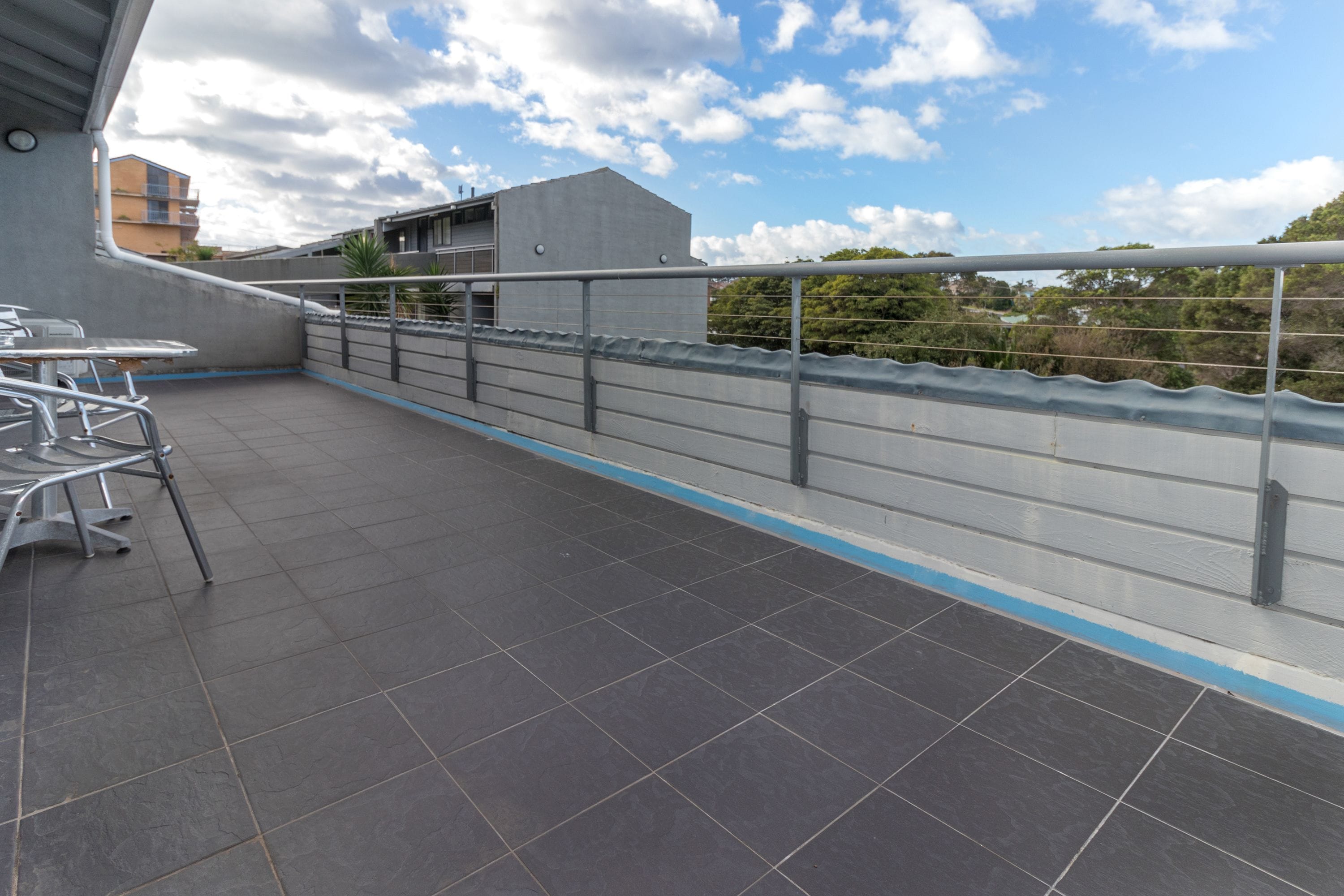 A rooftop terrace with a railing, a table, and chairs.