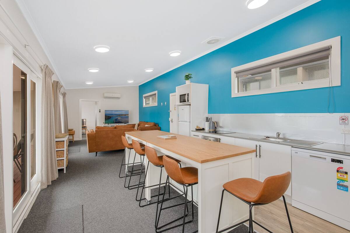 A modern kitchen with a blue accent wall, a wooden dining table, and bar stools.