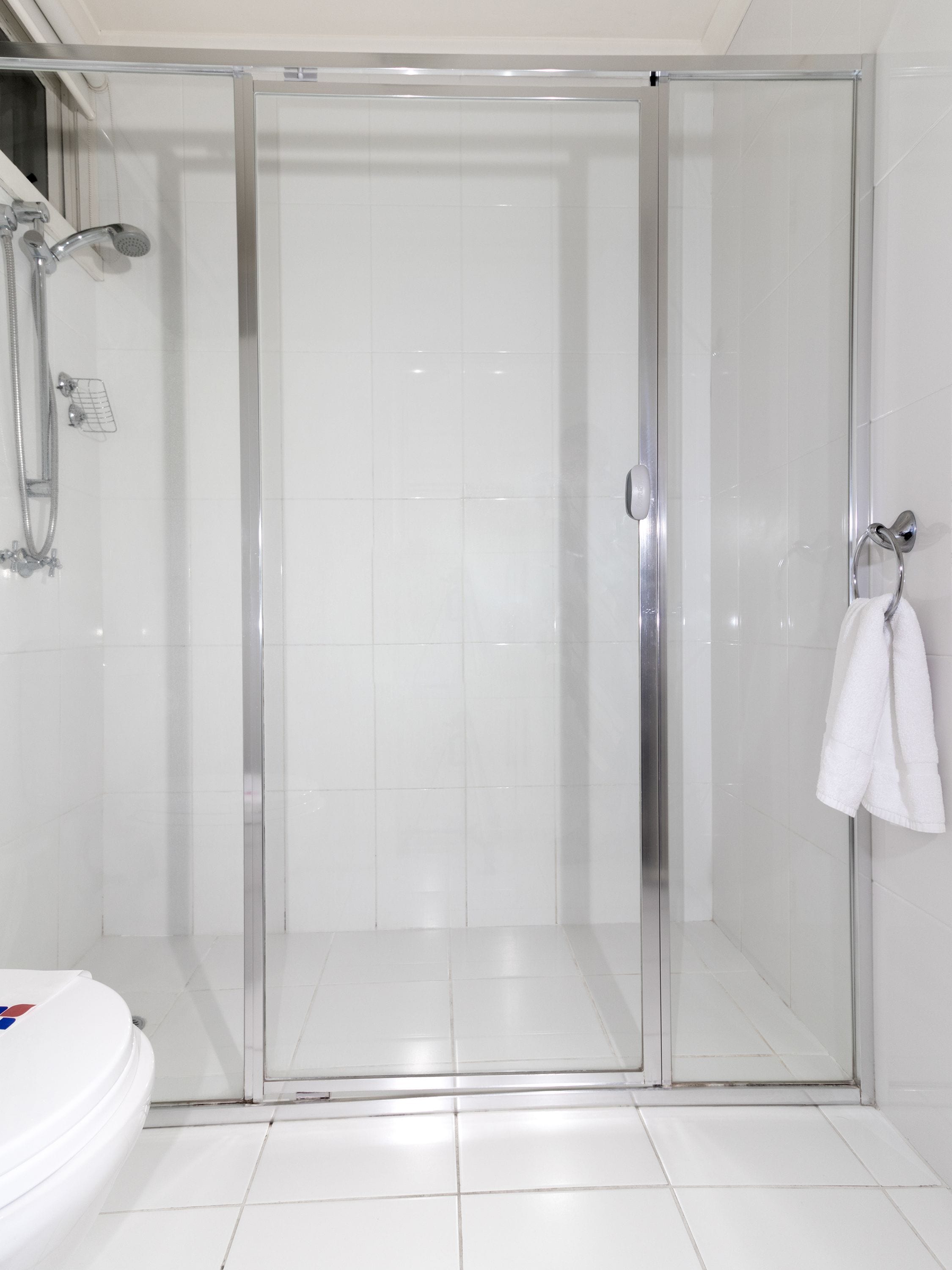 A glass-enclosed shower stall with a white tiled floor and a white toilet visible to the left.