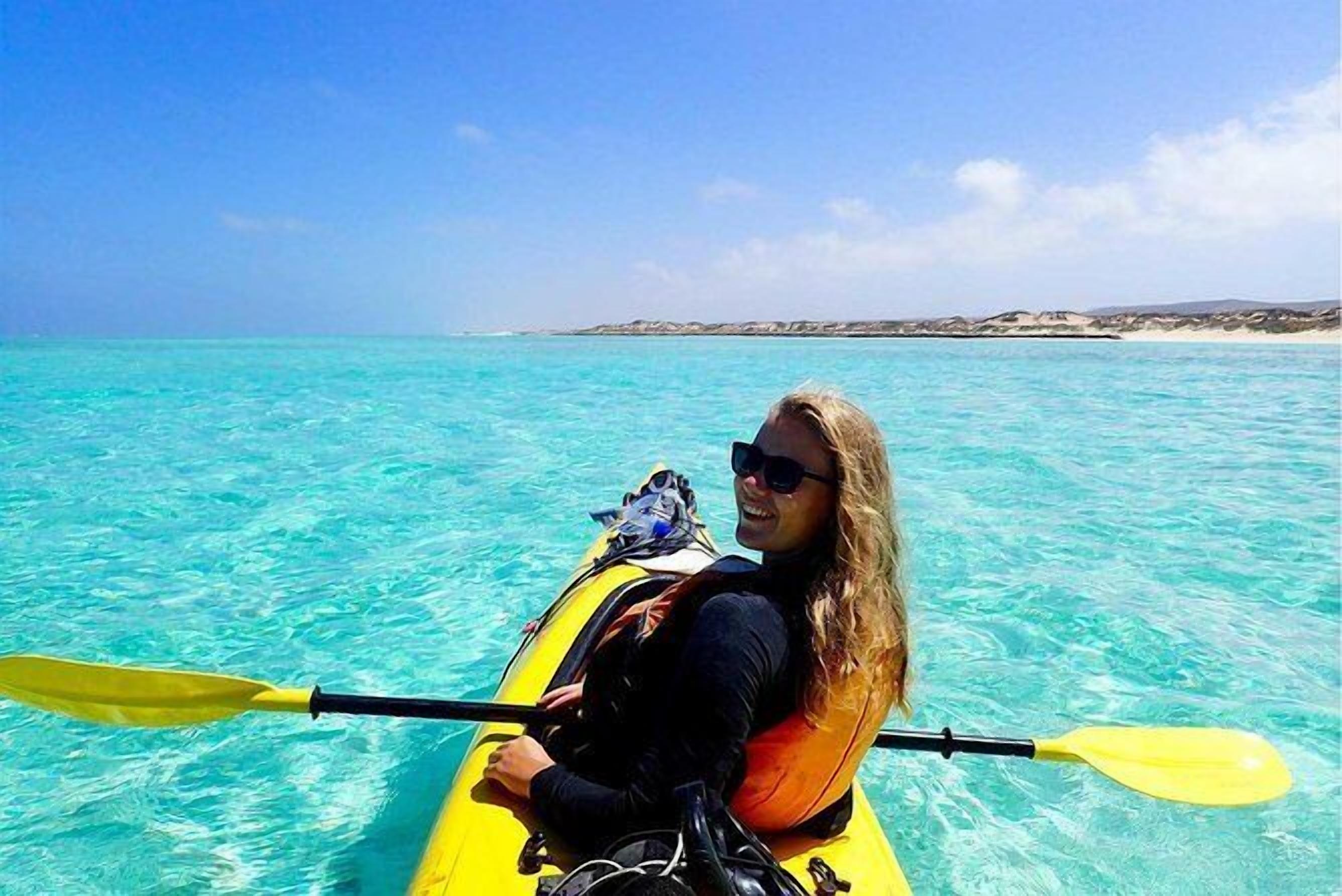 Eine Person sitzt in einem gelben Kajak auf klarem türkisblauem Wasser.