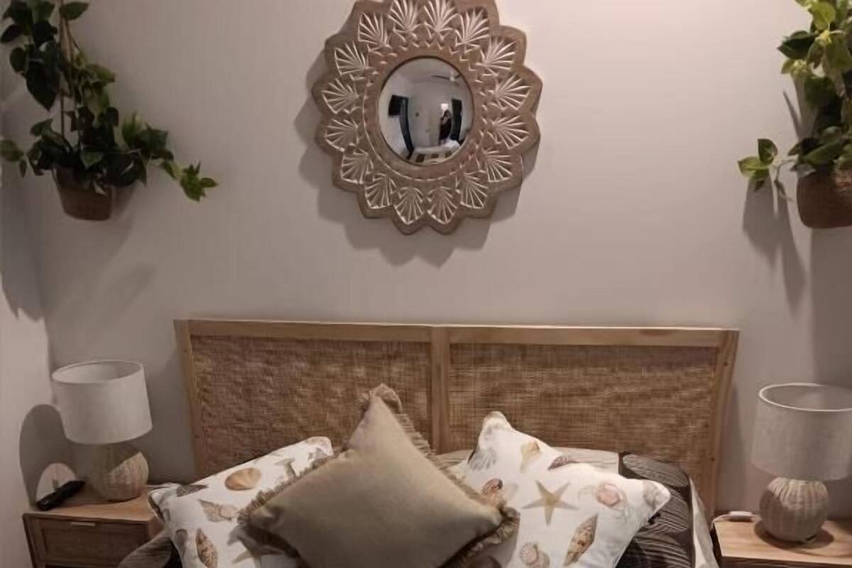 A bed with a patterned bedspread, two pillows, a headboard, bedside tables with lamps, and a wall-mounted mirror.