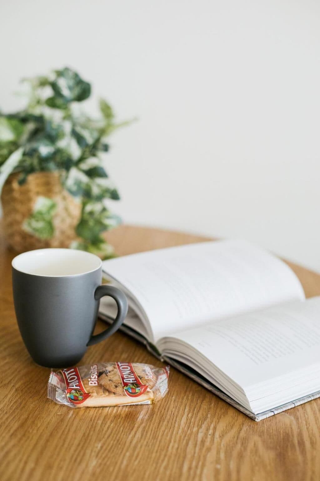 A book, a mug, and a packet of biscuits on a wooden table.