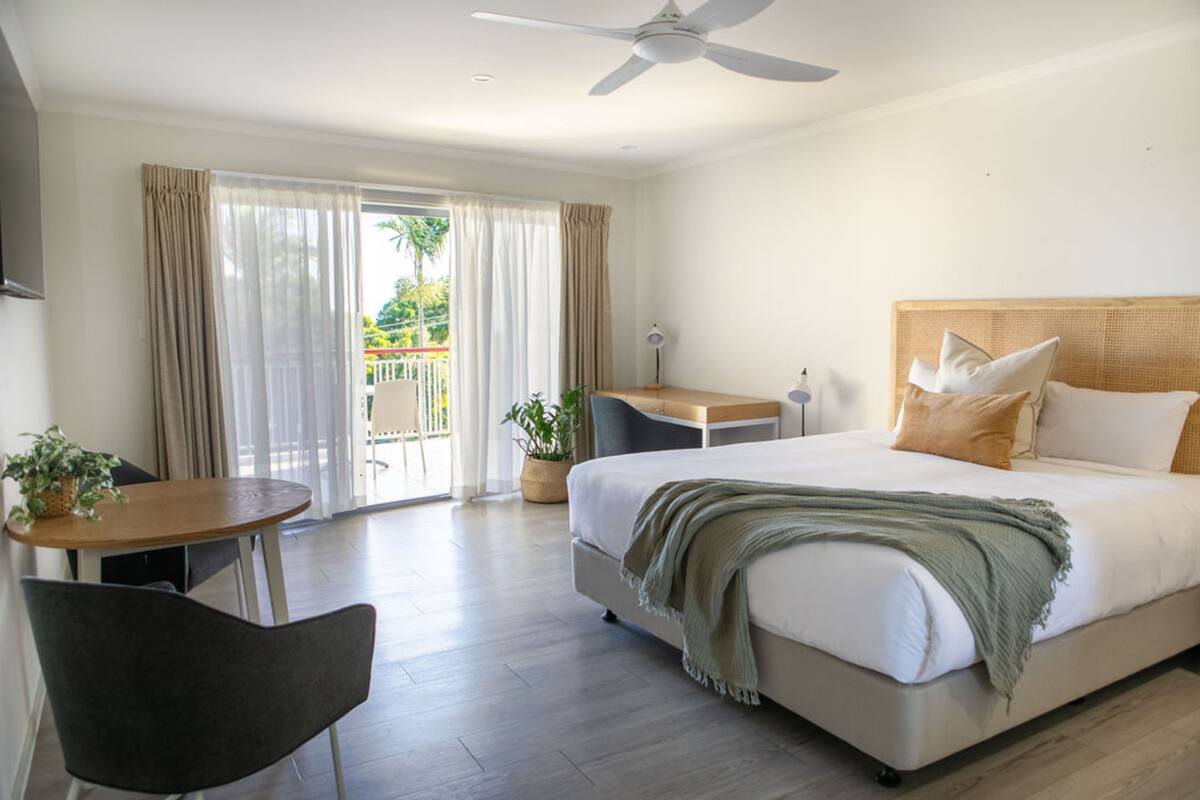 A hotel room with a bed, a desk, a chair, and a balcony with curtains.