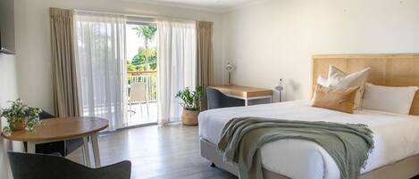 Habitación de hotel con cama, escritorio, silla y balcón con cortinas.