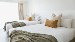 Habitació d'hotel amb dos llits, cortines beix i un panell de fons blanc.