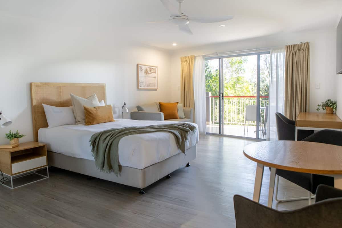 A hotel room with a bed, a desk, a chair, a balcony, and a ceiling fan.