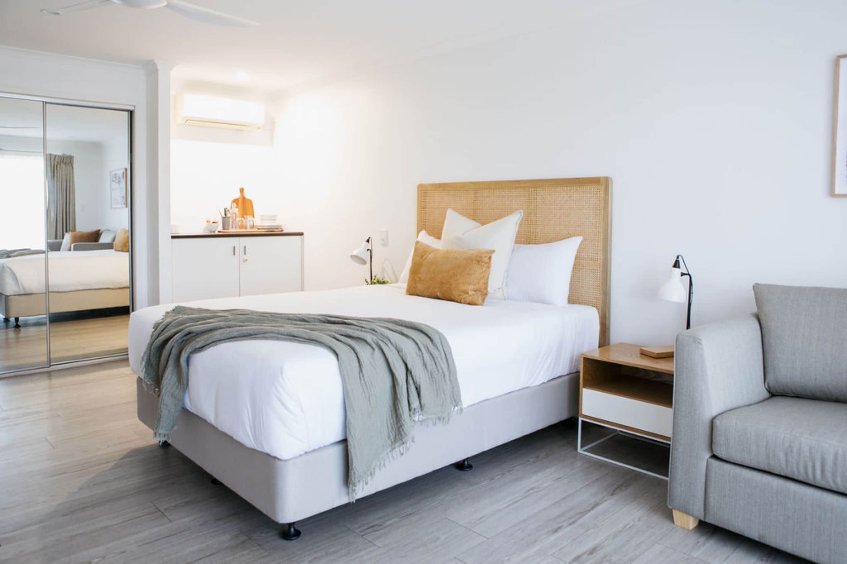 Een moderne hotelkamer met een groot bed, een grijze bank, een nachtkastje en een spiegel.
