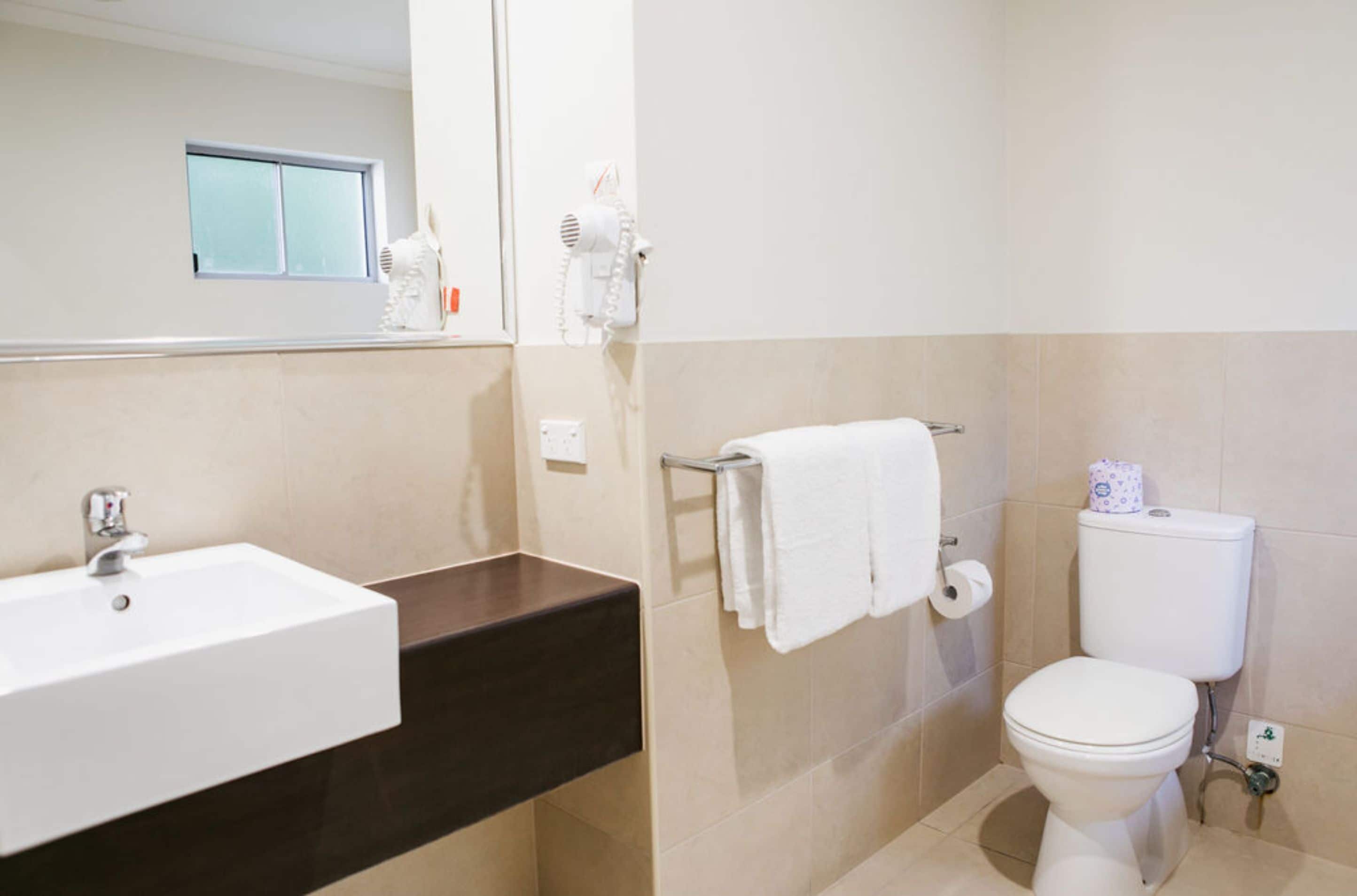 A bathroom with a white sink, dark countertop, towel rack, toilet, and a mirror.