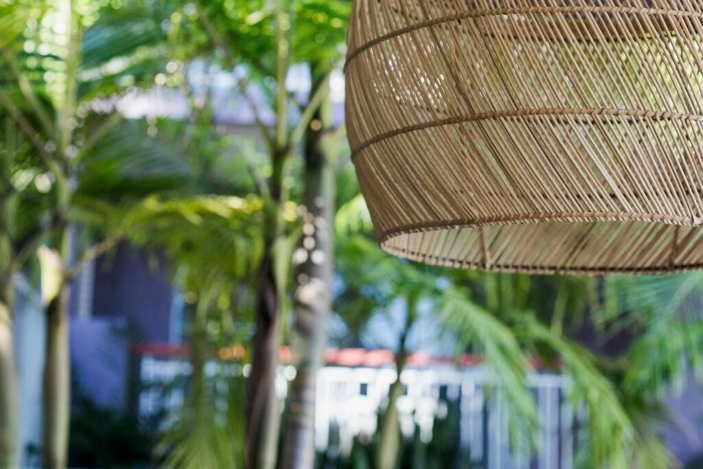 A hanging woven basket light fixture in a lush, green outdoor setting.