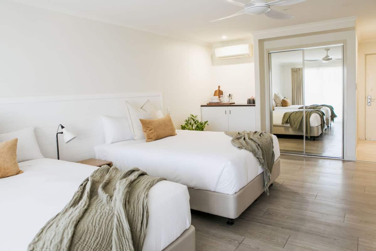 A hotel room with two beds, a desk, a mirror, and a sliding door leading to another room.