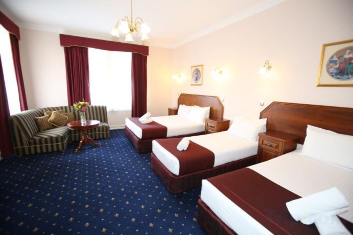 A hotel room with two single beds, a sofa, a small table, and a large window with curtains.
