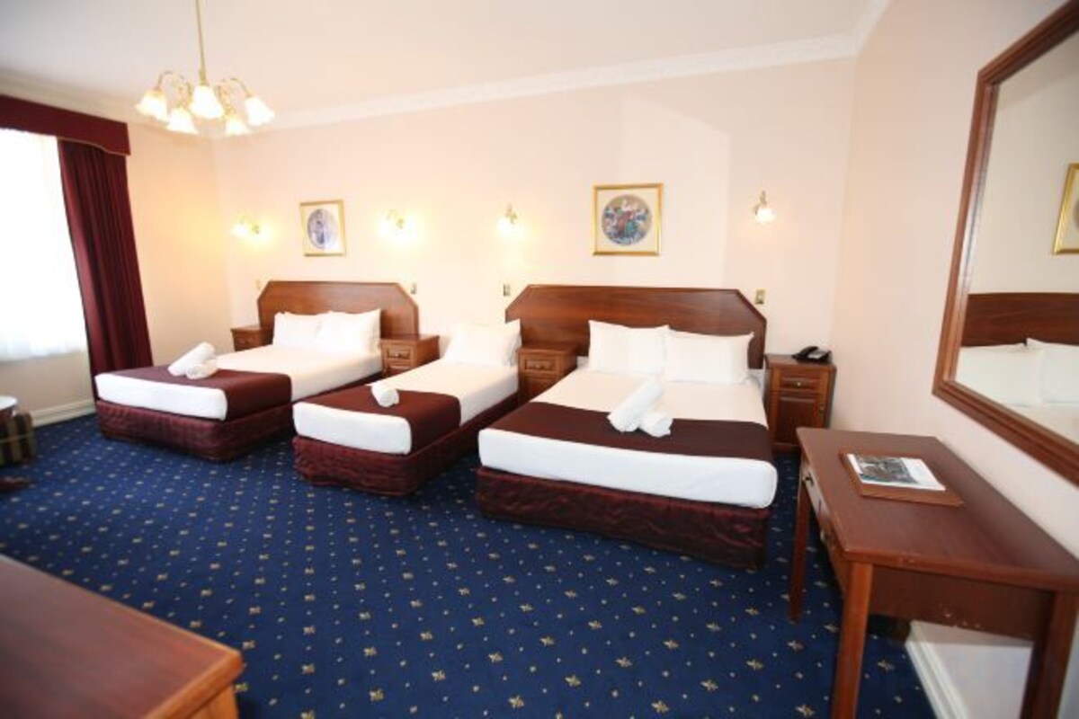 A hotel room with two beds, a desk, a chair, a dresser, and a large mirror.