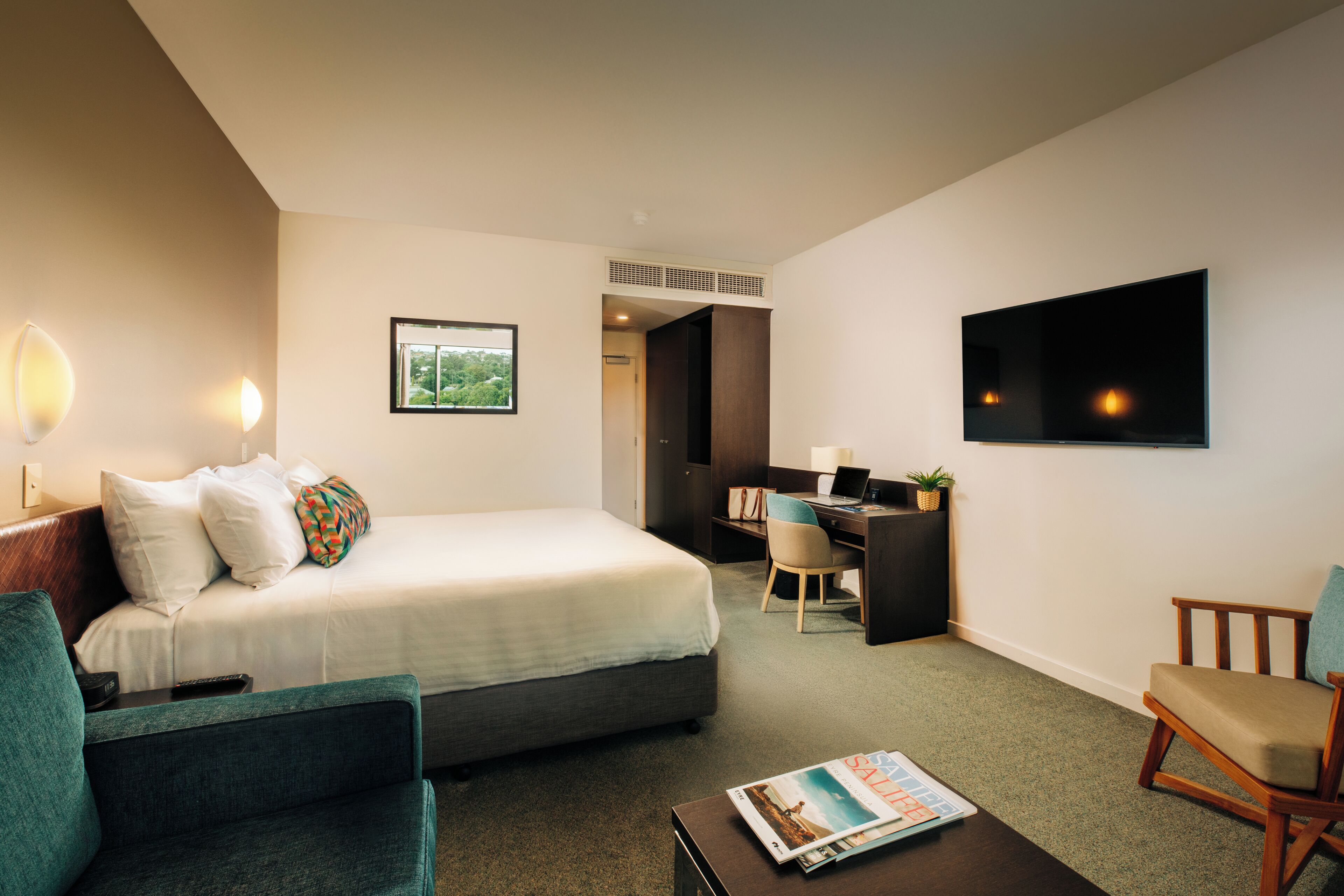 Een hotelkamer met een bed, een bureau, een televisie, een stoel en een salontafel.