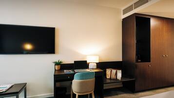 A hotel room with a bed, a desk with a laptop, a chair, a TV mounted on the wall, and a wardrobe.
