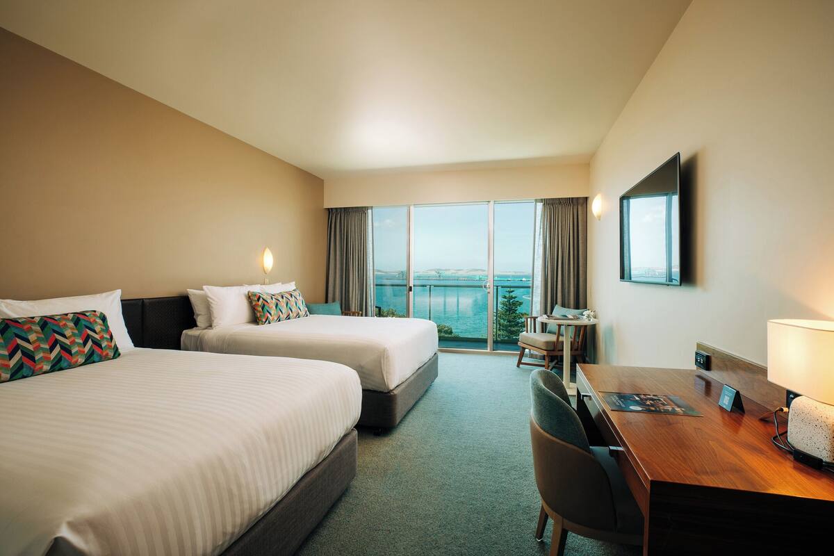 Ein Hotelzimmer mit zwei Betten, einem Schreibtisch, einem Sessel, einem Fernseher und Blick ins Freie.