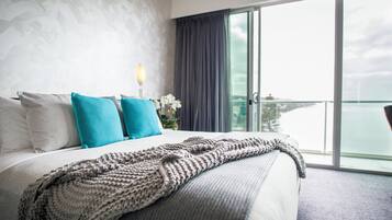 A hotel room with a large bed, a view of the city, and a balcony with a view of the water.