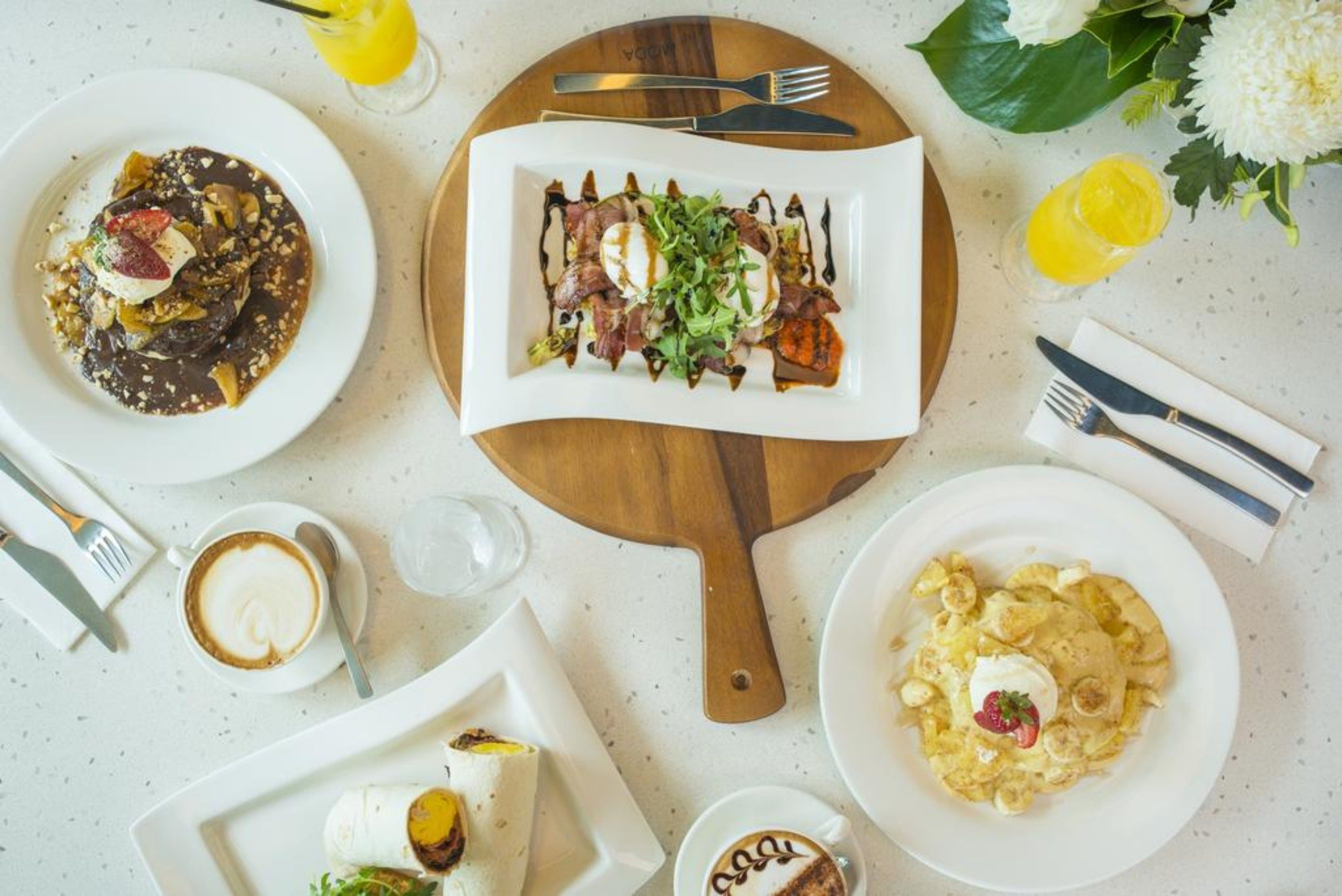 A dining table with plates of food, a wooden board, and cutlery.