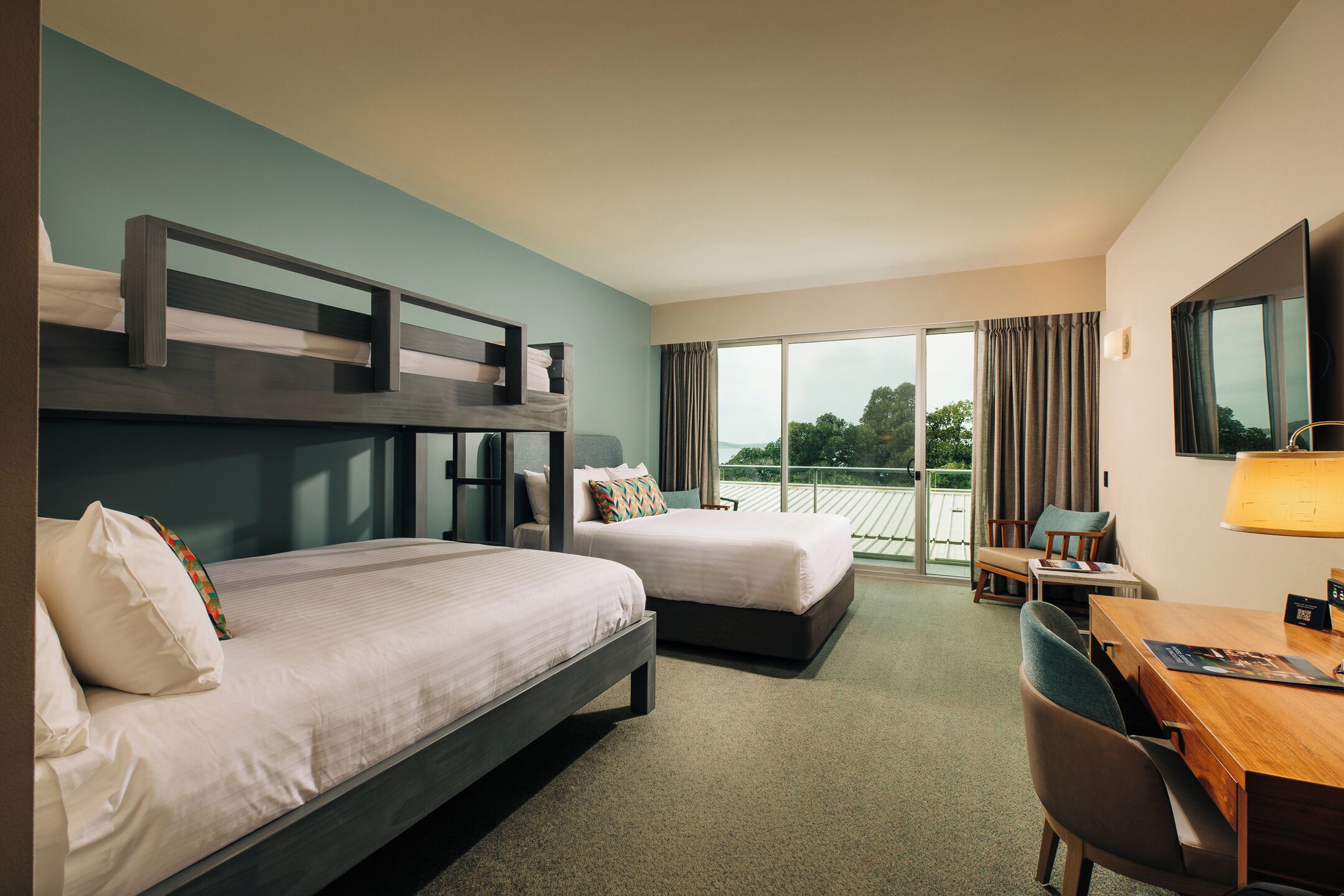 Ein Hotelzimmer mit zwei Betten, einem Schreibtisch, einem Stuhl und einem großen Fenster mit Vorhängen.