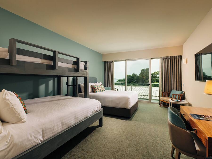Ein Hotelzimmer mit zwei Betten, einem Schreibtisch, einem Stuhl und einem großen Fenster mit Vorhängen.