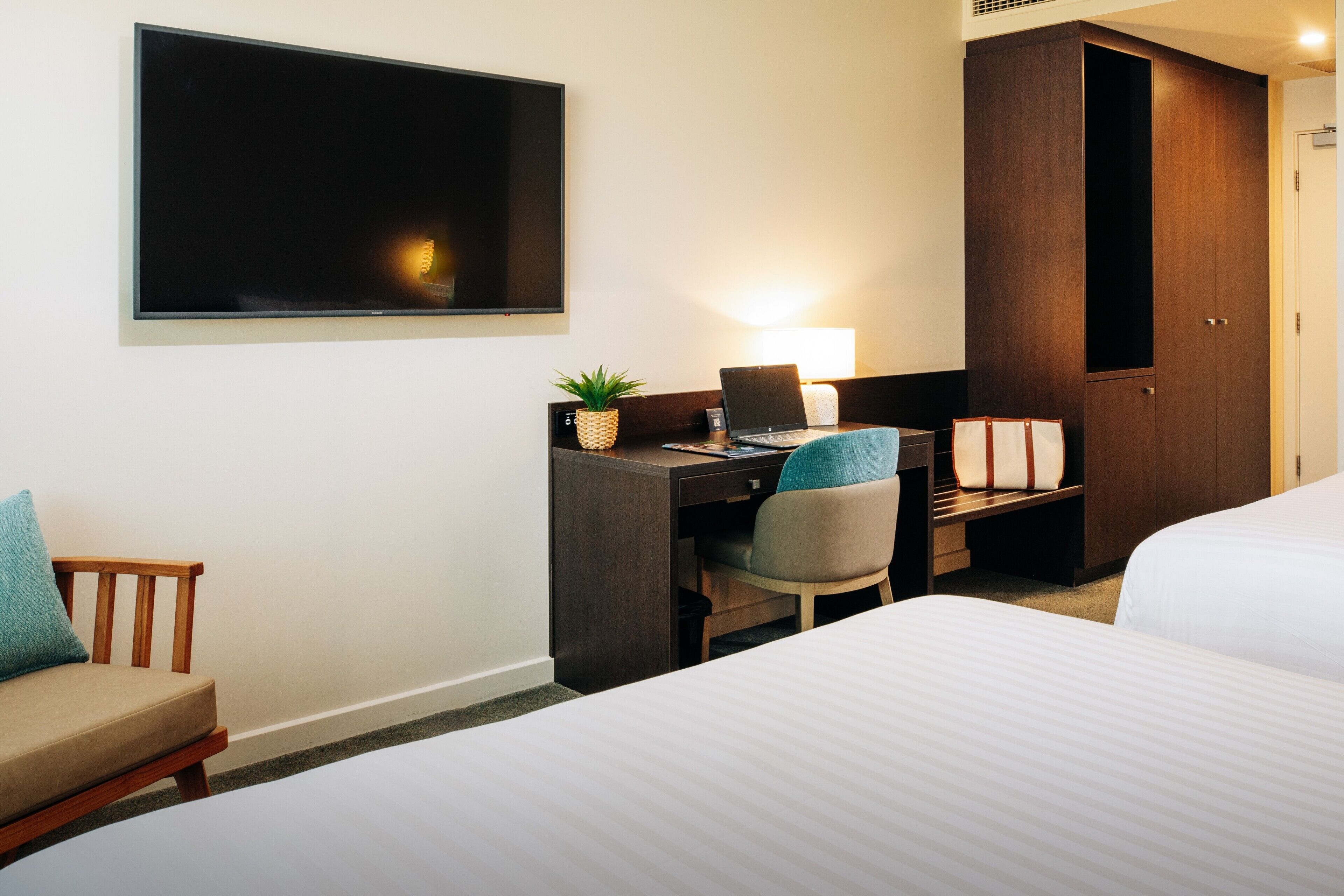 A hotel room with a bed, a desk with a laptop, a chair, a TV, and a wardrobe.