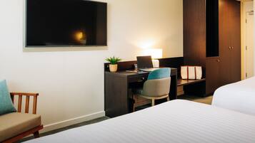 A hotel room with a bed, a desk with a laptop, a chair, a TV, and a wardrobe.