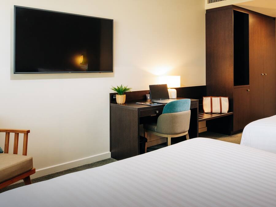 A hotel room with a bed, a desk with a laptop, a chair, a TV, and a wardrobe.