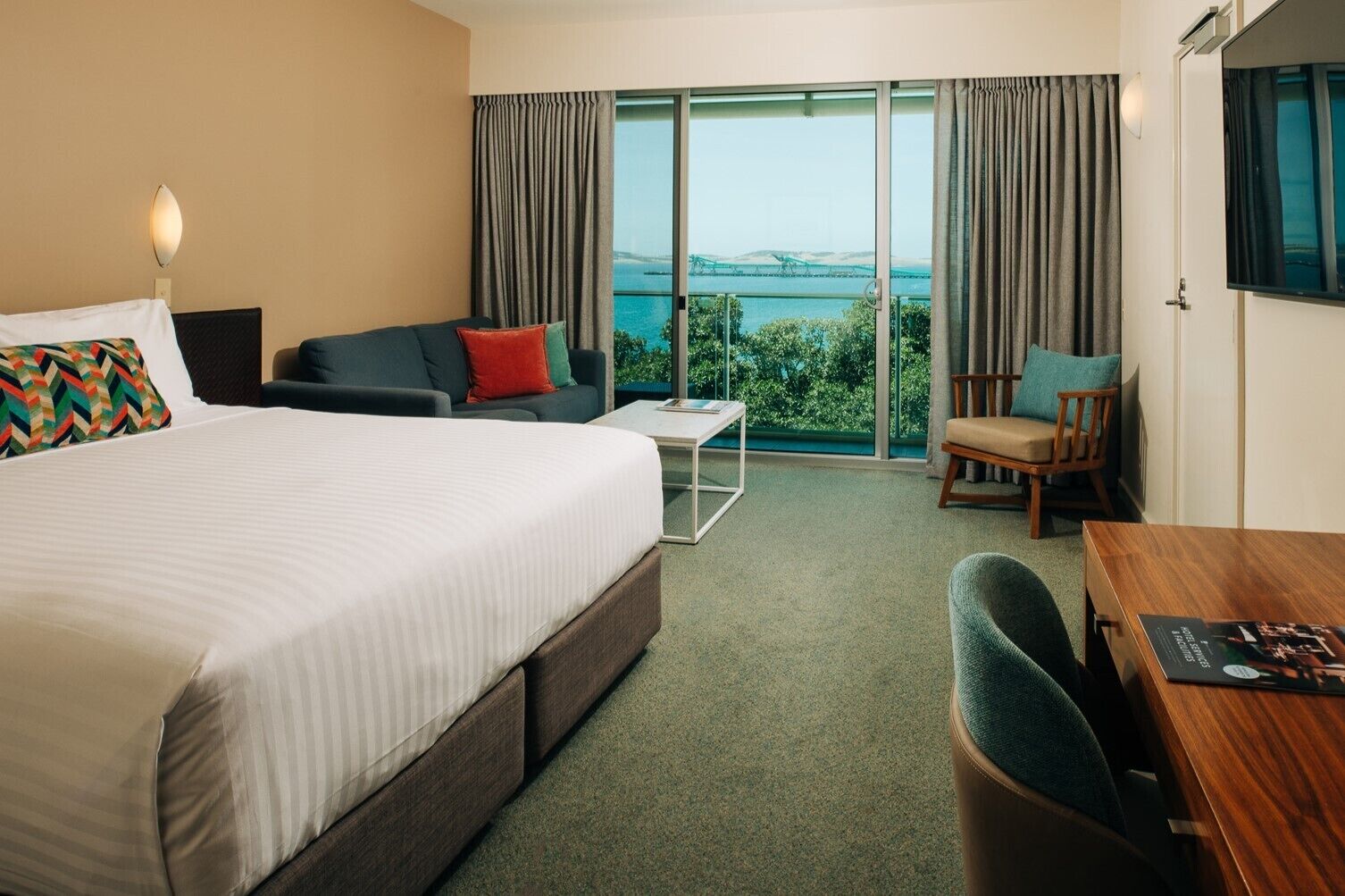 Habitación de hotel con cama, sofá, sillón, una mesita y televisor.