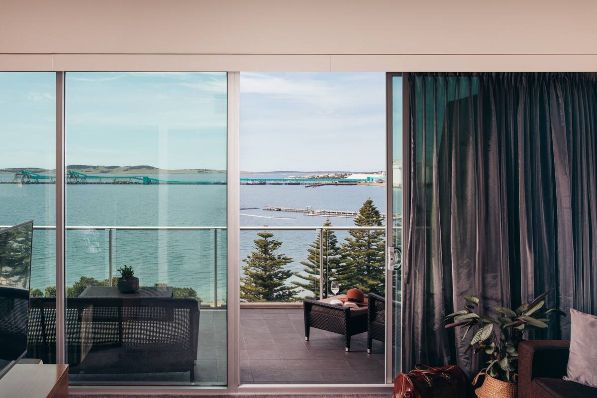 Ein Balkon mit Blick auf eine Brücke über dem Wasser, ein Stuhl, ein Tisch mit einer Pflanze und eine Sitzecke.