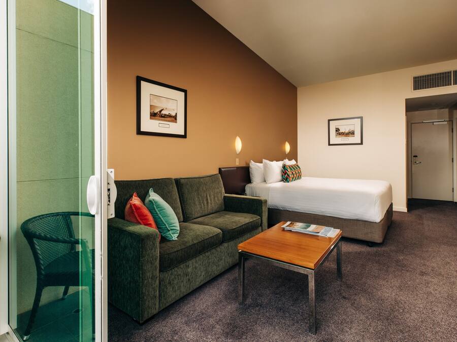 A hotel room with a bed, a sofa, a coffee table, and a chair.