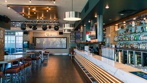 Uma área de bar com um balcão comprido, vários bancos e uma seleção variada de bebidas.