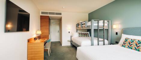A hotel room with a desk, two beds, a mirror, and a door leading to a bathroom.