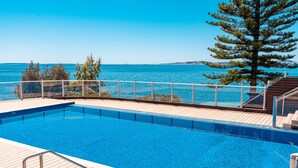 Piscina com deck de madeira e vista para o mar.