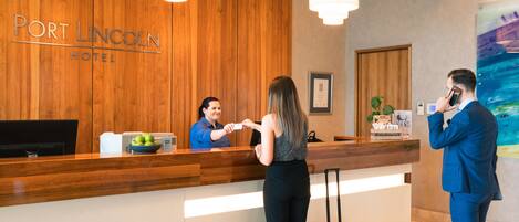 Un mostrador de recepción de hotel con un panel de pared de madera, una pantalla digital y un frutero.