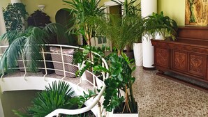 A spacious indoor area with a white metal railing, multiple potted plants, a patterned floor, and a wooden cabinet. - Vila Elat (Chisinau)