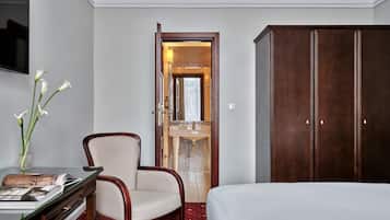 Una camera d'albergo con un letto, una scrivania con un vaso di fiori, una sedia, un armadio e un bagno visibile attraverso una porta aperta.