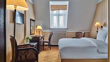 Una habitación de hotel con cama, escritorio, silla, lámpara y ventana con cortinas.