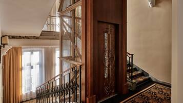 Una imponente escalera con barandales de metal ornamentados, un suelo con motivos y una puerta de madera con un panel decorativo.