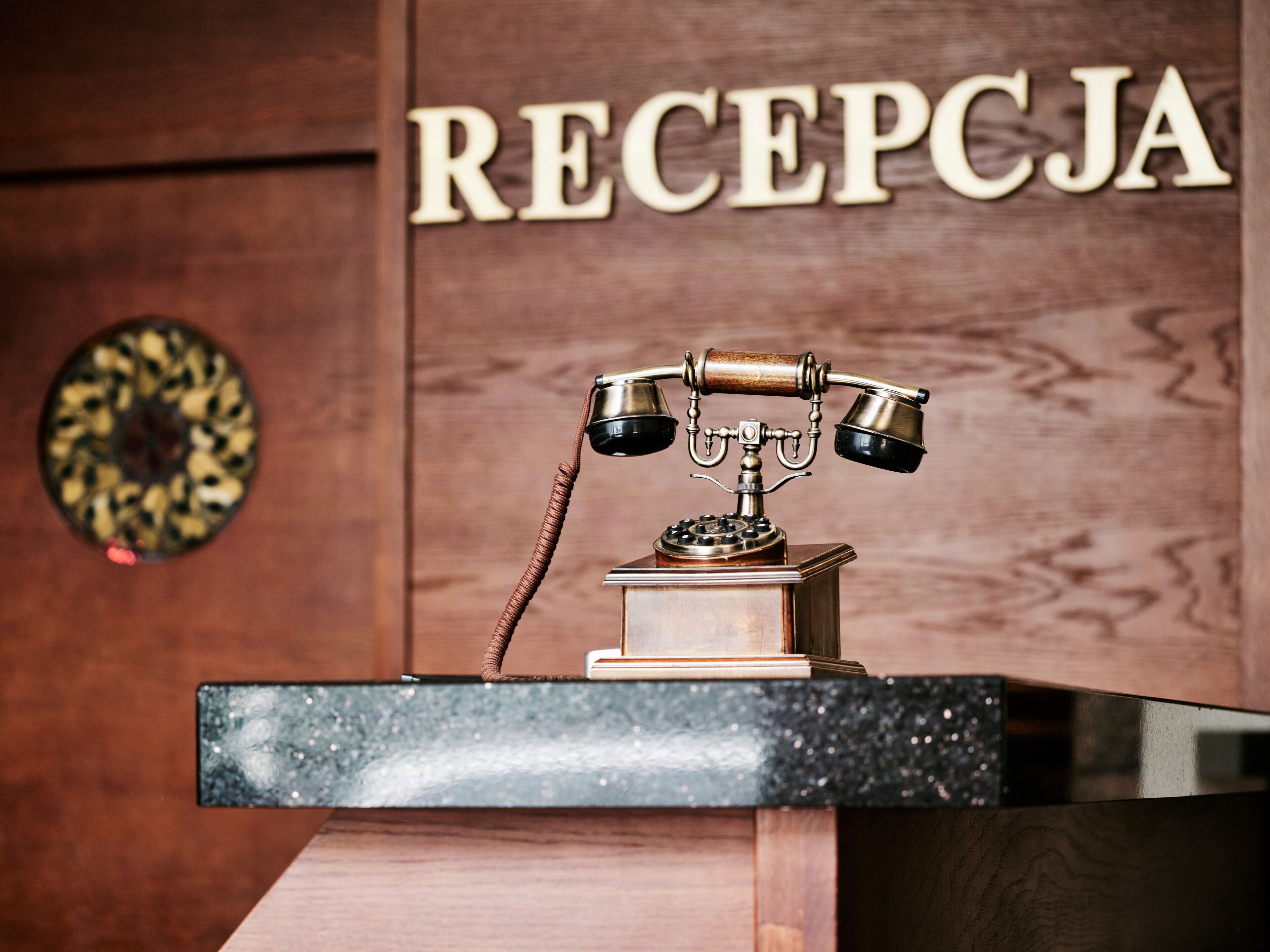 A wooden reception desk with a vintage telephone and a sign that reads 'RECEPCJA'.