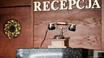 A wooden reception desk with a vintage telephone and a sign that reads 'RECEPCJA'.