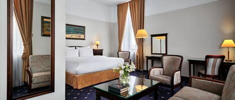 A hotel room with a bed, two armchairs, a sofa, a coffee table, and a desk.