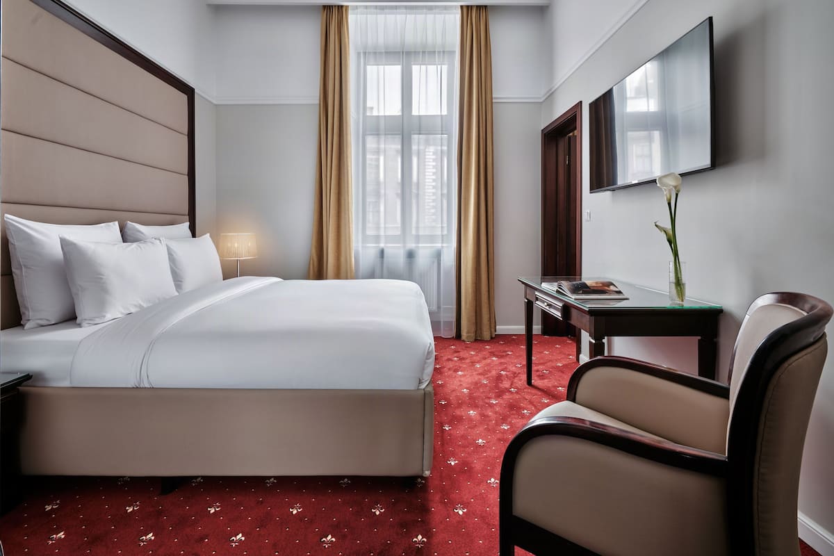 Habitación de hotel con cama, escritorio, silla, televisor y ventana con cortinas.
