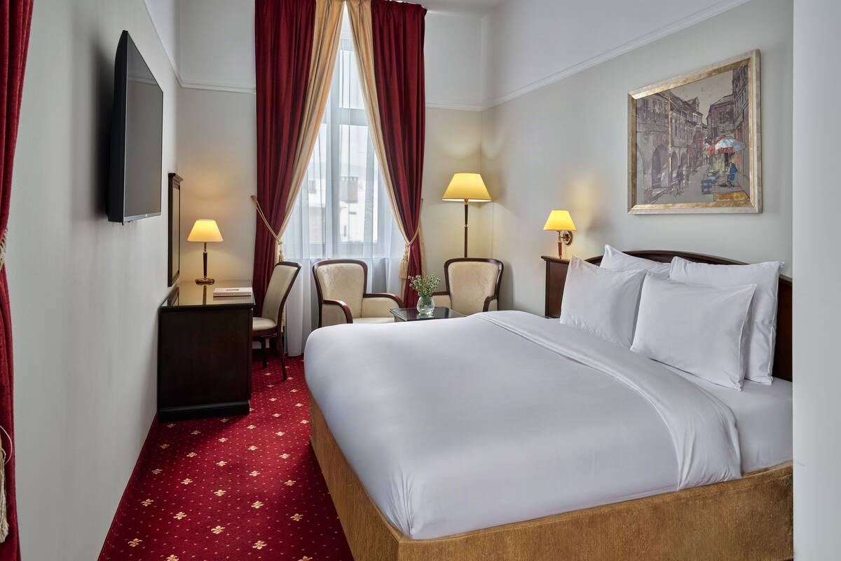 Habitación de hotel con una cama grande, dos sillas, un escritorio, un televisor y un cuadro en la pared.